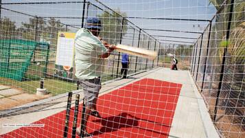 A net cricket practice area with a red mat, a batting cage, and a green storage unit.