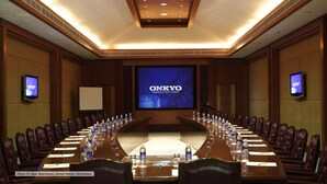 Un salón de conferencias con una larga mesa, sillas y una pantalla grande que muestra 