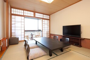 A traditional Japanese room with tatami flooring, a low table, cushions, a TV, and a sliding door. - Hotel Kikunoya (Hatsukaichi)
