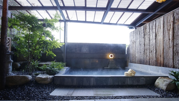A traditional Japanese-style hot spring bath area with stone steps, a wooden wall, and a stone bench. - Hotel Kikunoya (Hatsukaichi)