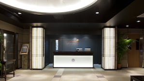 A hotel reception area with a modern design, featuring a reception desk, a large illuminated sign, and a potted plant. - Hotel Kikunoya (Hatsukaichi)