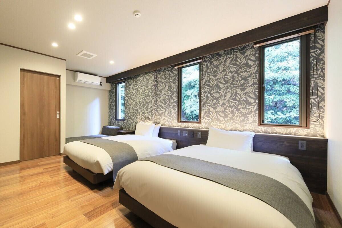 A bedroom with two beds, a wooden floor, a large window, and a wall-mounted air conditioner.