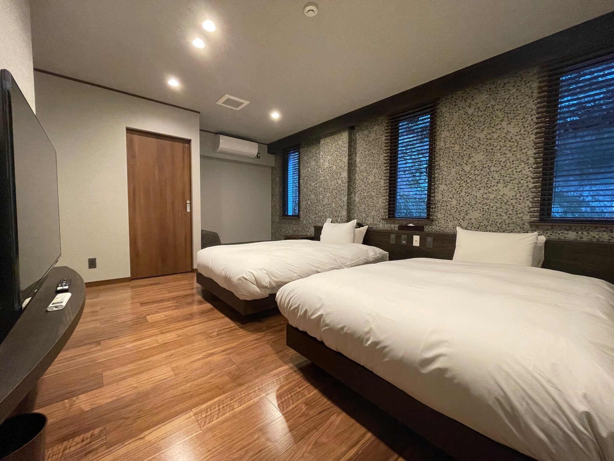 A hotel room with two beds, a TV, and an air conditioning unit.