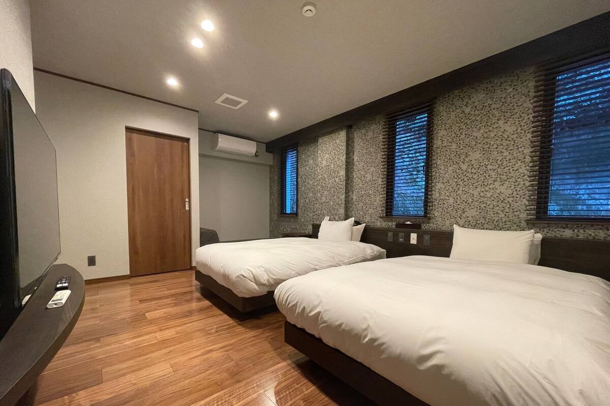 A hotel room with two beds, a TV, and an air conditioning unit.