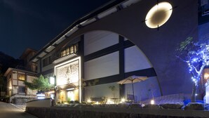 A modern building with a large illuminated archway, outdoor seating area, and a well-lit entrance. - Hotel Kikunoya (Hatsukaichi)