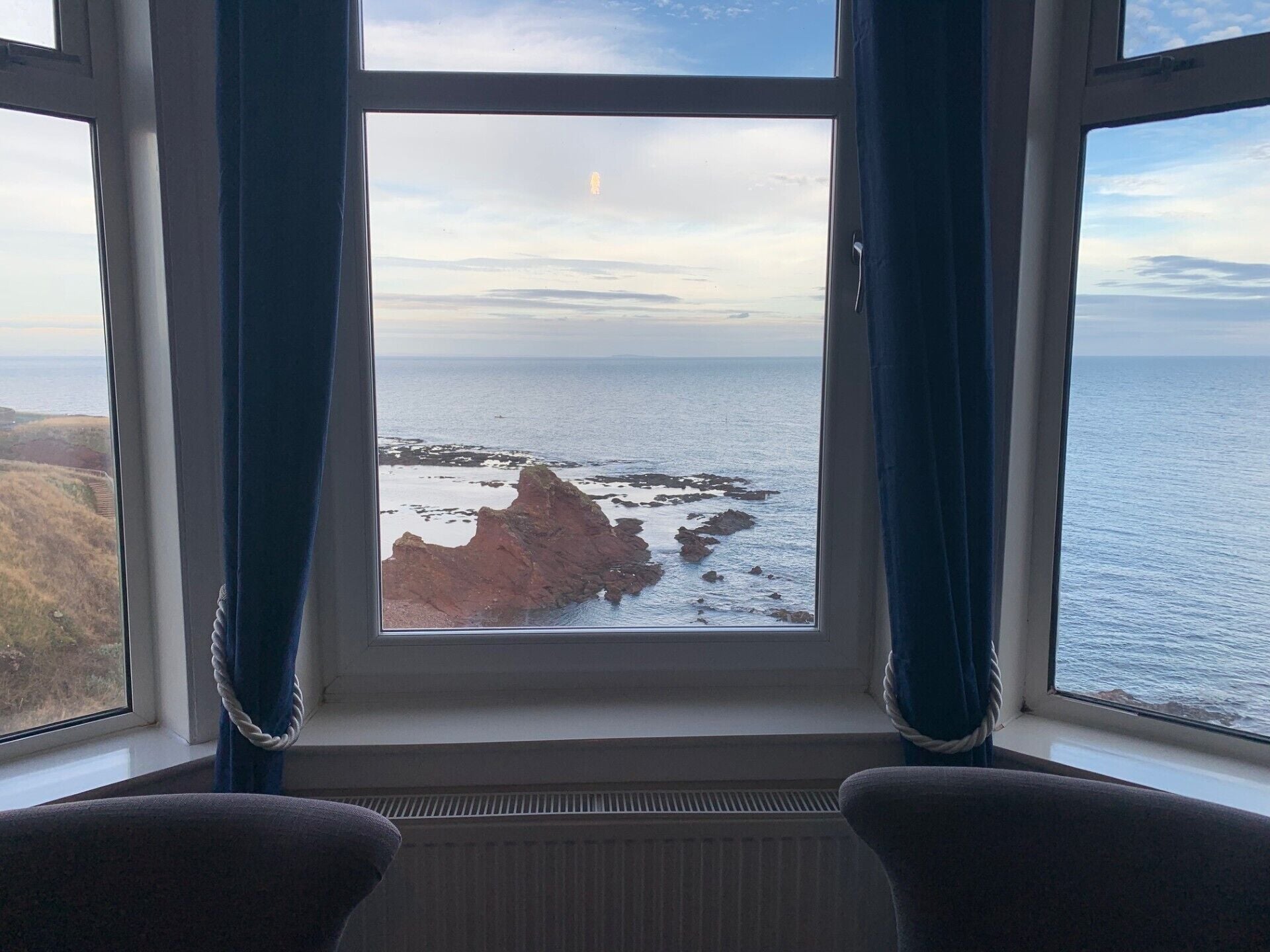A room with a large window overlooking a rocky coastline and the sea.