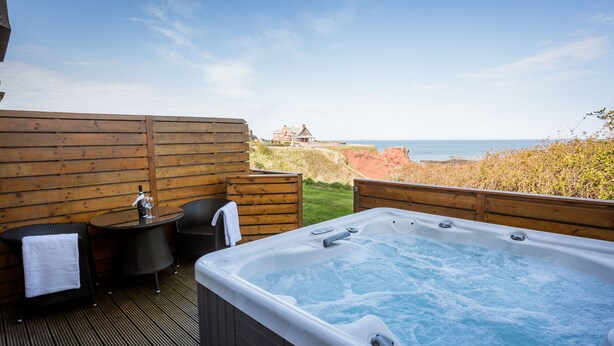 A wooden deck with a hot tub, two wicker chairs, and a small table with a towel. - Bayswell Park Hotel (Dunbar)
