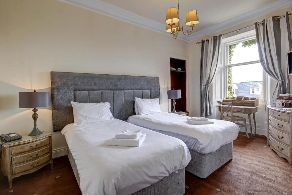 Quarto de hotel com duas camas, uma escrivaninha e um aparador.