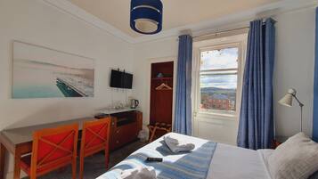 A hotel room with a bed, a desk with a chair, a television, a window with curtains, and a painting on the wall.