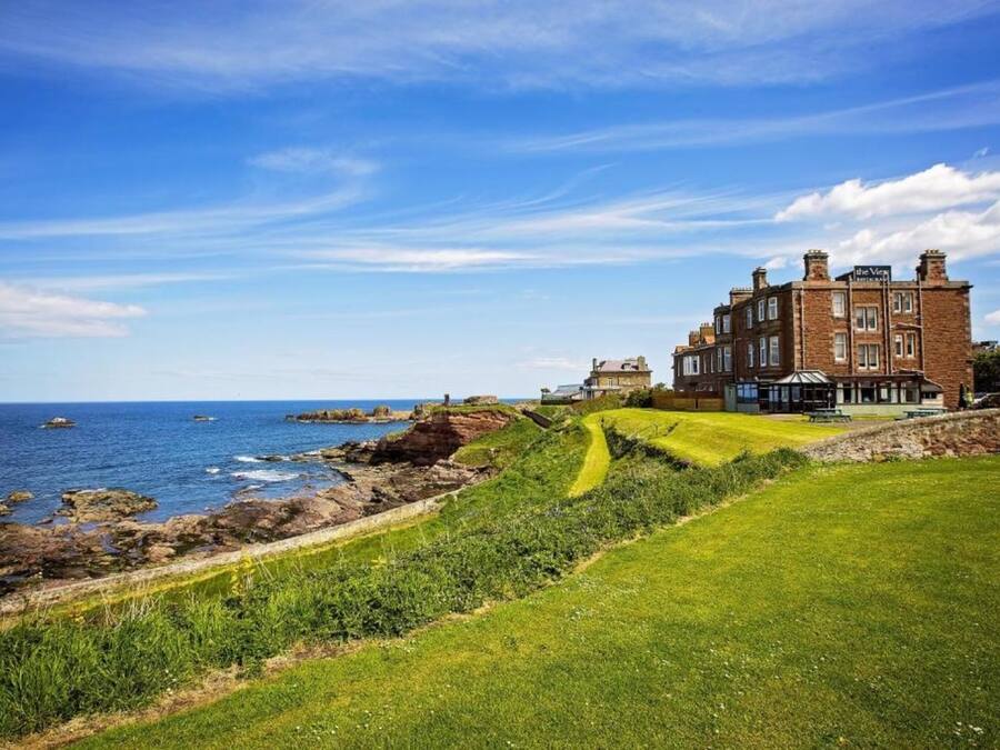 A coastal hotel with a prominent brick building, a grassy lawn, and a view of the sea.