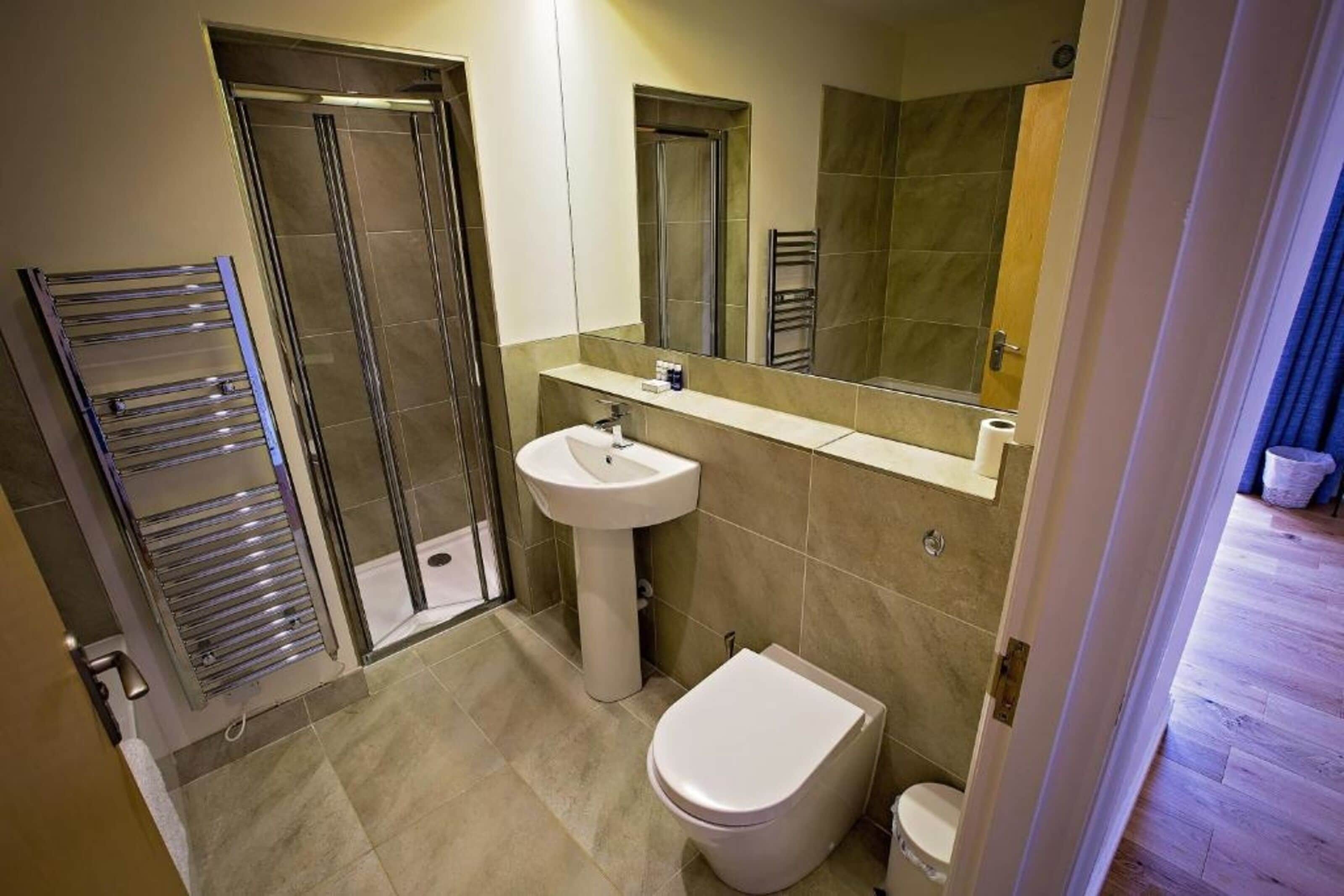 Un baño con cabina de ducha de vidrio, lavamanos pedestal, inodoro y perchero para toallas.