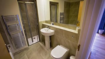 Un baño con cabina de ducha de vidrio, lavamanos pedestal, inodoro y perchero para toallas.