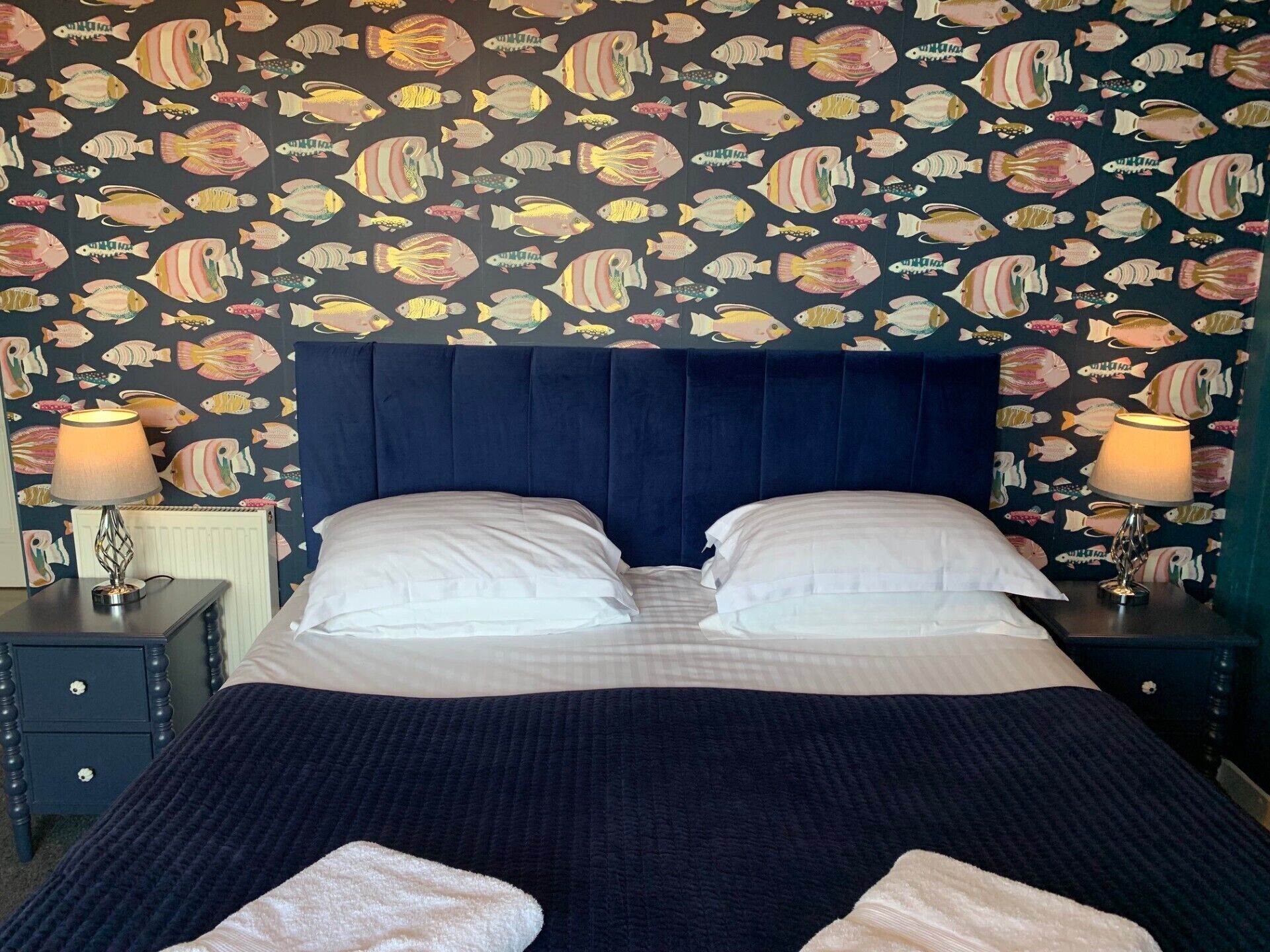 A bedroom with a bed, two bedside tables, and a wall with a fish pattern.