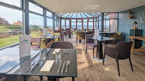 A restaurant with a glass table and chairs, a wine list sign, and a view of the sea. - Bayswell Park Hotel (Dunbar)