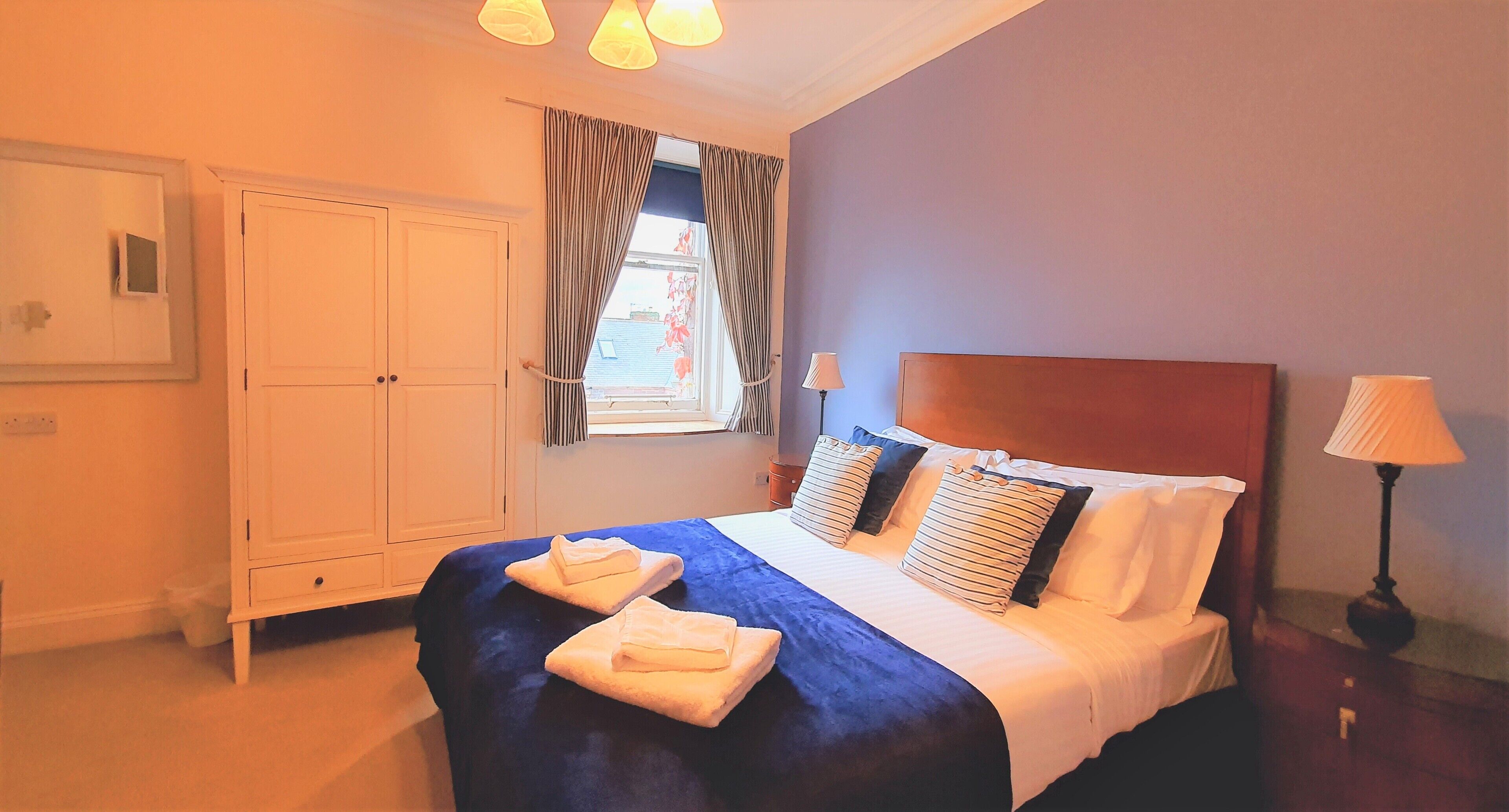 Una habitación de hotel con una cama, un armario, una ventana con cortinas y dos lámparas de noche.