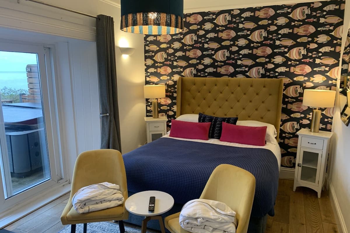 Quarto de hotel com cama grande, duas cadeiras, mesa pequena e varanda com mesa e cadeiras.