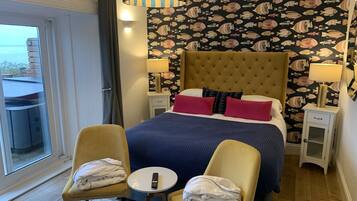 A hotel room with a large bed, two chairs, a small table, and a balcony with a table and chairs.