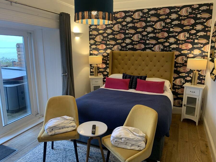 A hotel room with a large bed, two chairs, a small table, and a balcony with a table and chairs.
