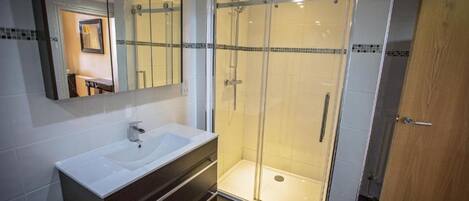 Un baño moderno con ducha acristalada, un lavabo grande de color blanco y una puerta de madera.