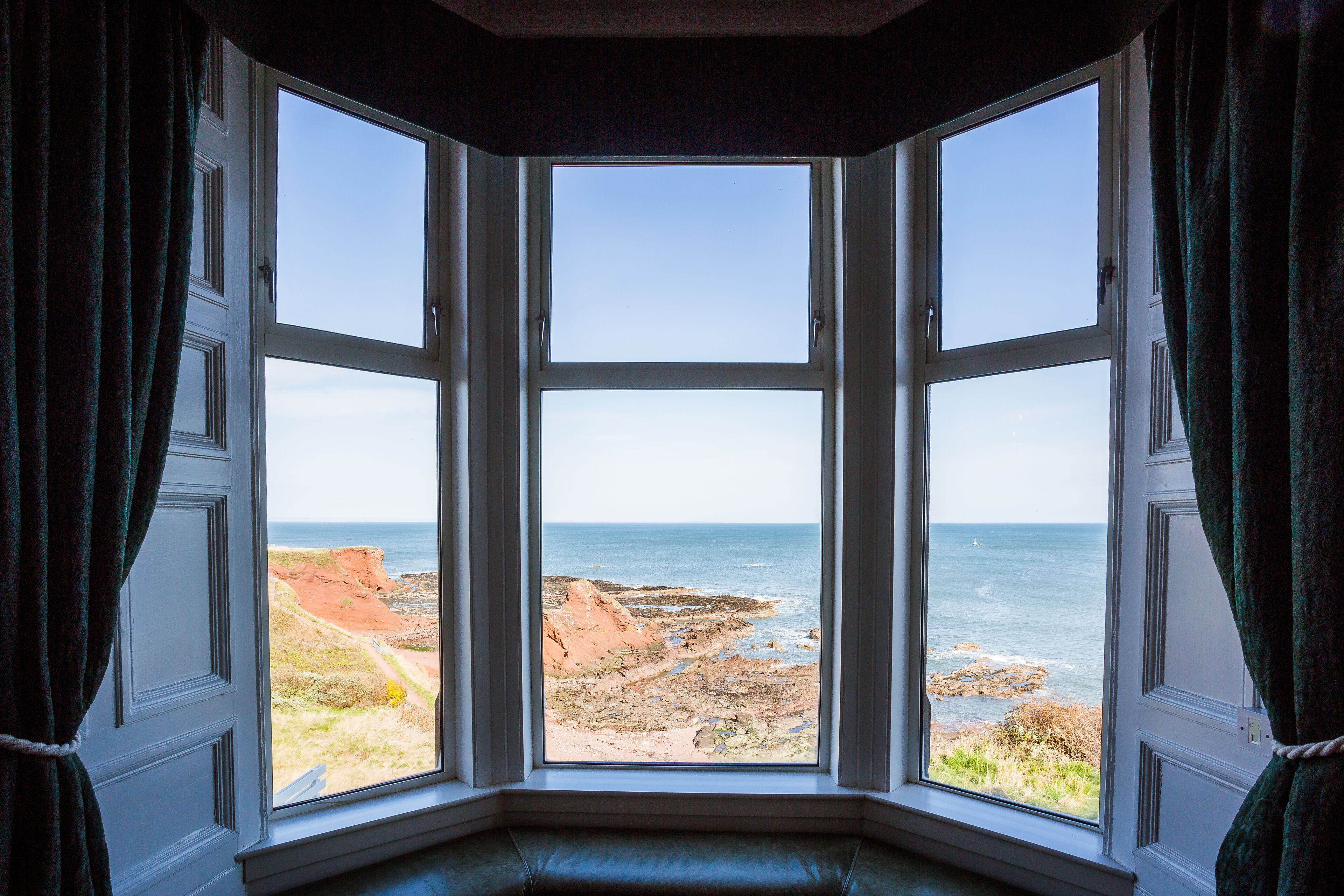 A bay window with a view of a rocky coastline and the sea.