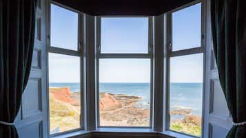 A bay window with a view of a rocky coastline and the sea.