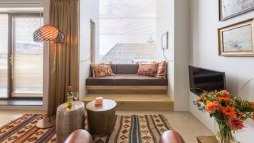 Een gezellige woonkamer met een bank, een televisie, een bloevas en een kamerkleed met patroon.