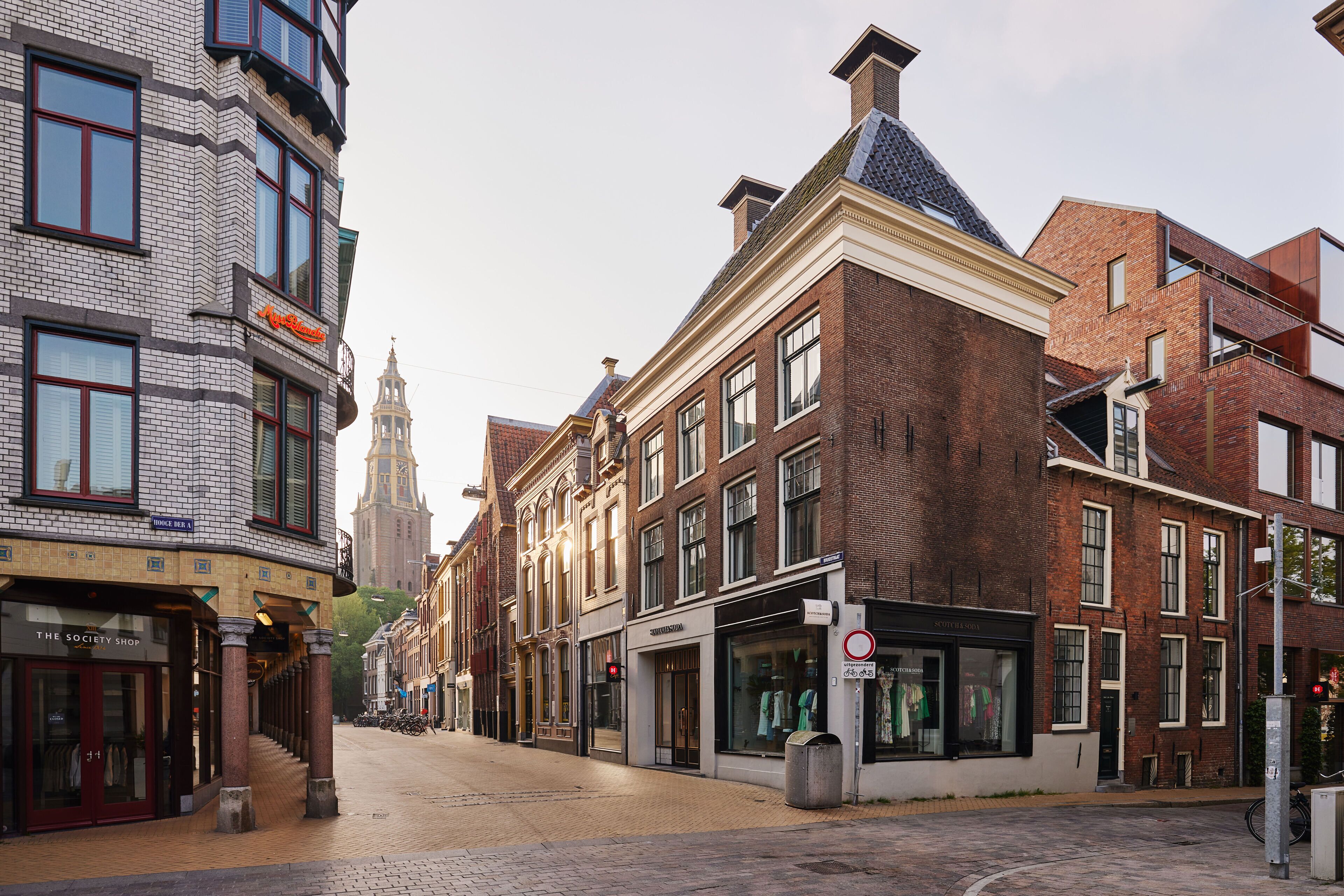Une rue bordée de bâtiments historiques, surmontée d’un imposant beffroi et pavée de pierres.
