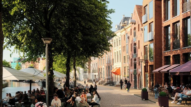 A cobblestone street lined with brick buildings, outdoor seating areas, and a canal in the background. - Hotel Miss Blanche (Groningen)