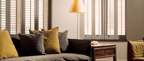 A modern living room with a sofa, pillows, a lamp, and a window with blinds.