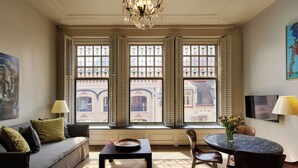 A room with a sofa, a table with a bowl, a chair, a lamp, and a window with shutters. - Hotel Miss Blanche (Groningen)