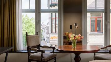 A room with a dining table, chairs, a vase with flowers, and large windows with curtains.