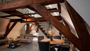 An attic room with exposed wooden beams, a round wooden table with chairs, a sofa, and a staircase. - Hotel Miss Blanche (Groningen)