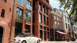 A vintage white convertible car parked on a cobblestone street in front of a brick building with a sign reading 'LIBAU.' - Hotel Miss Blanche (Groningen)