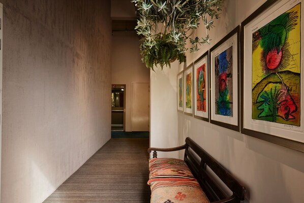 Un pasillo con un banco, obras de arte enmarcadas en la pared y una planta colgante.
