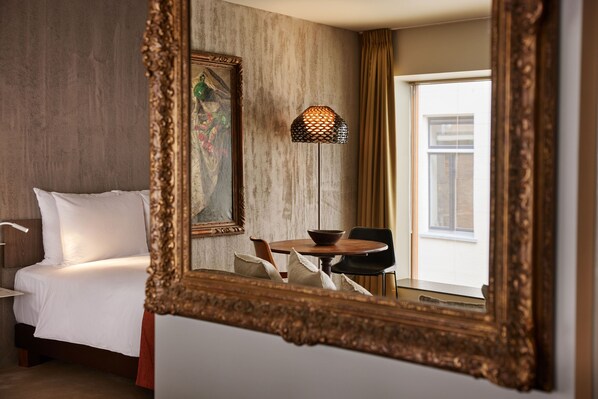 Habitación de hotel con cama, una mesa de comedor con sillas, un cuadro en la pared y un espejo grande.
