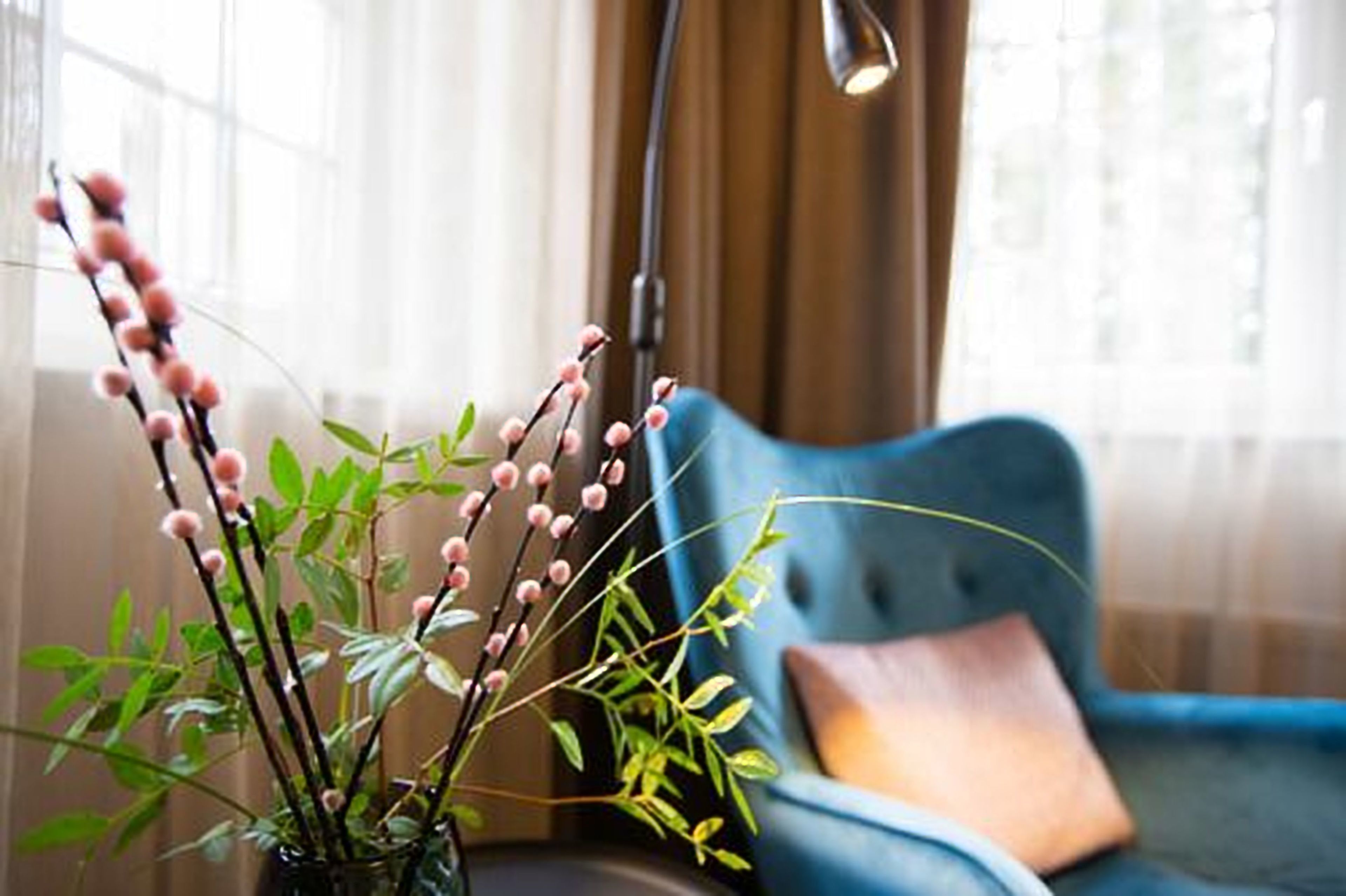 A room with a blue sofa and a vase with green plants and pink buds.