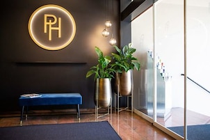 Un área de recepción con un banco, un letrero en la pared con 'PH' y dos plantas en macetas.