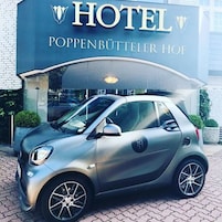 Un coche pequeño aparcado frente a un hotel con un cartel que dice 'HOTEL POPPENBÜTTERLER HOF'.