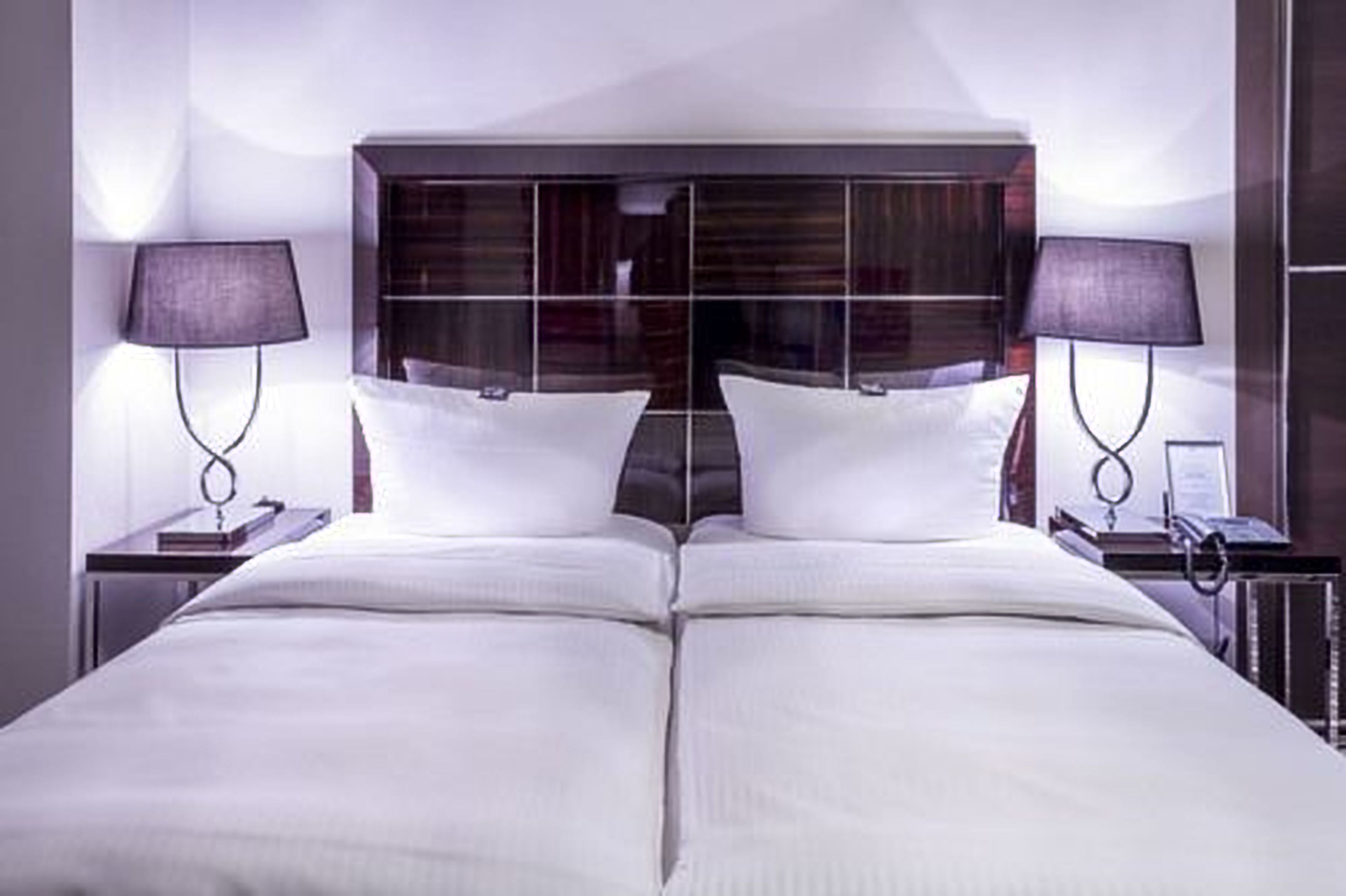 Ein Doppelbett mit dunklem Kopfteil, zwei Nachttische mit Lampen und ein Spiegel über dem Bett.