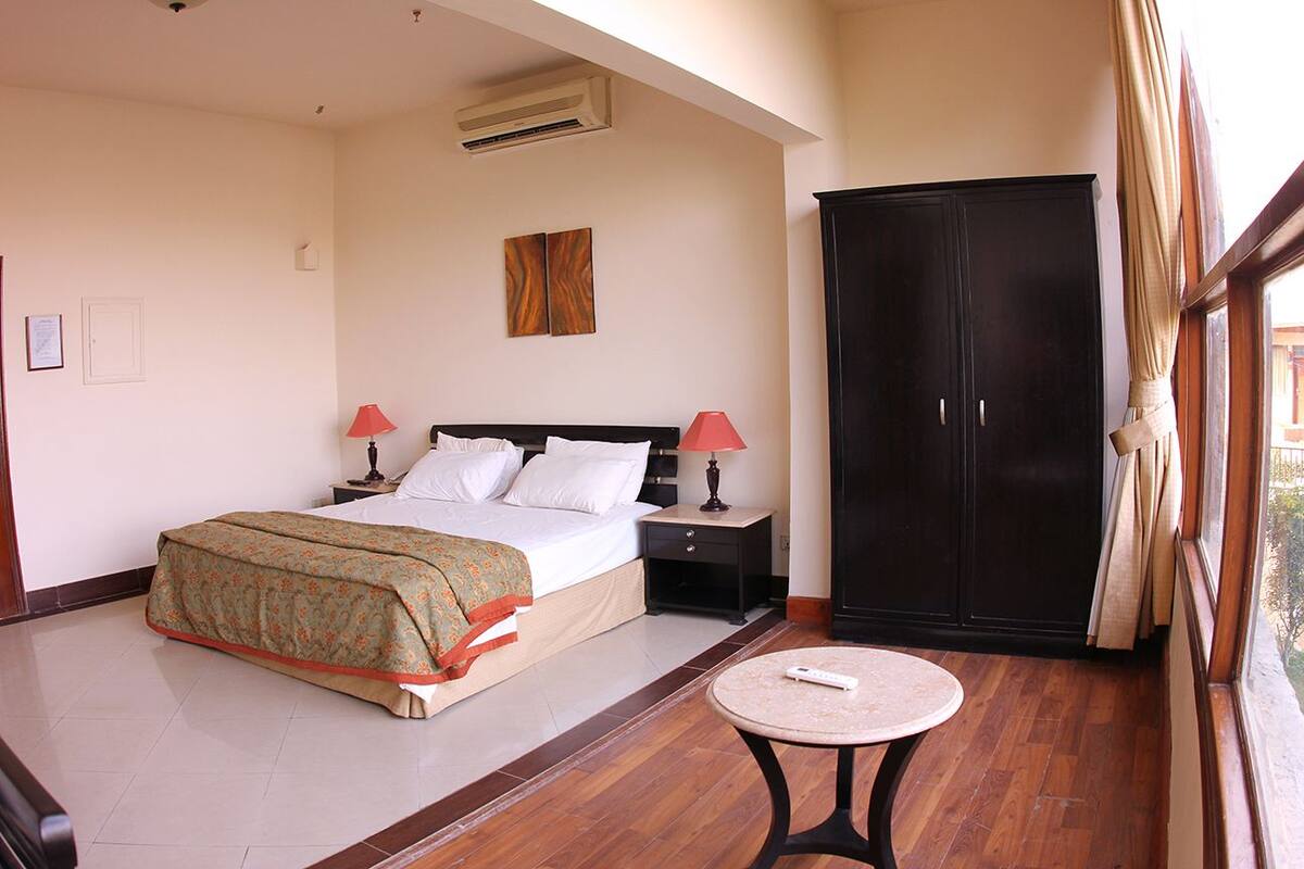 A hotel room with a bed, bedside tables, a wardrobe, a round table, and a window with curtains.