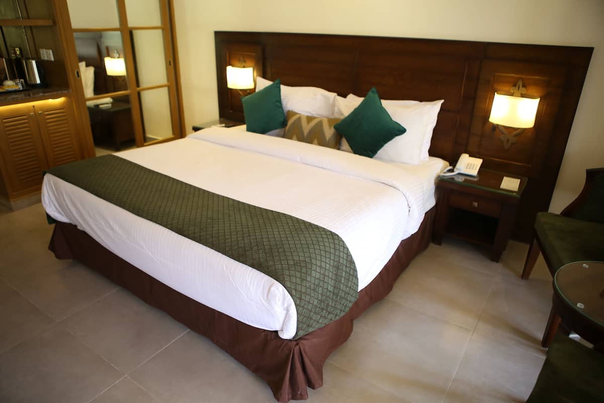 A hotel room with a large bed, wooden headboard, two bedside lamps, a nightstand, and a green chair.