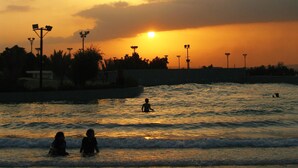 A sunset over a body of water with silhouettes of people and street lamps. - Dreamworld Resort, Hotel & Golf Course (Karachi)