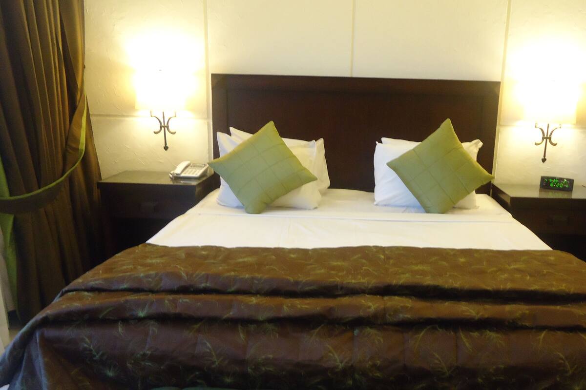 A hotel room with a large bed, two bedside tables, a nightstand, a telephone, and two wall-mounted lamps.