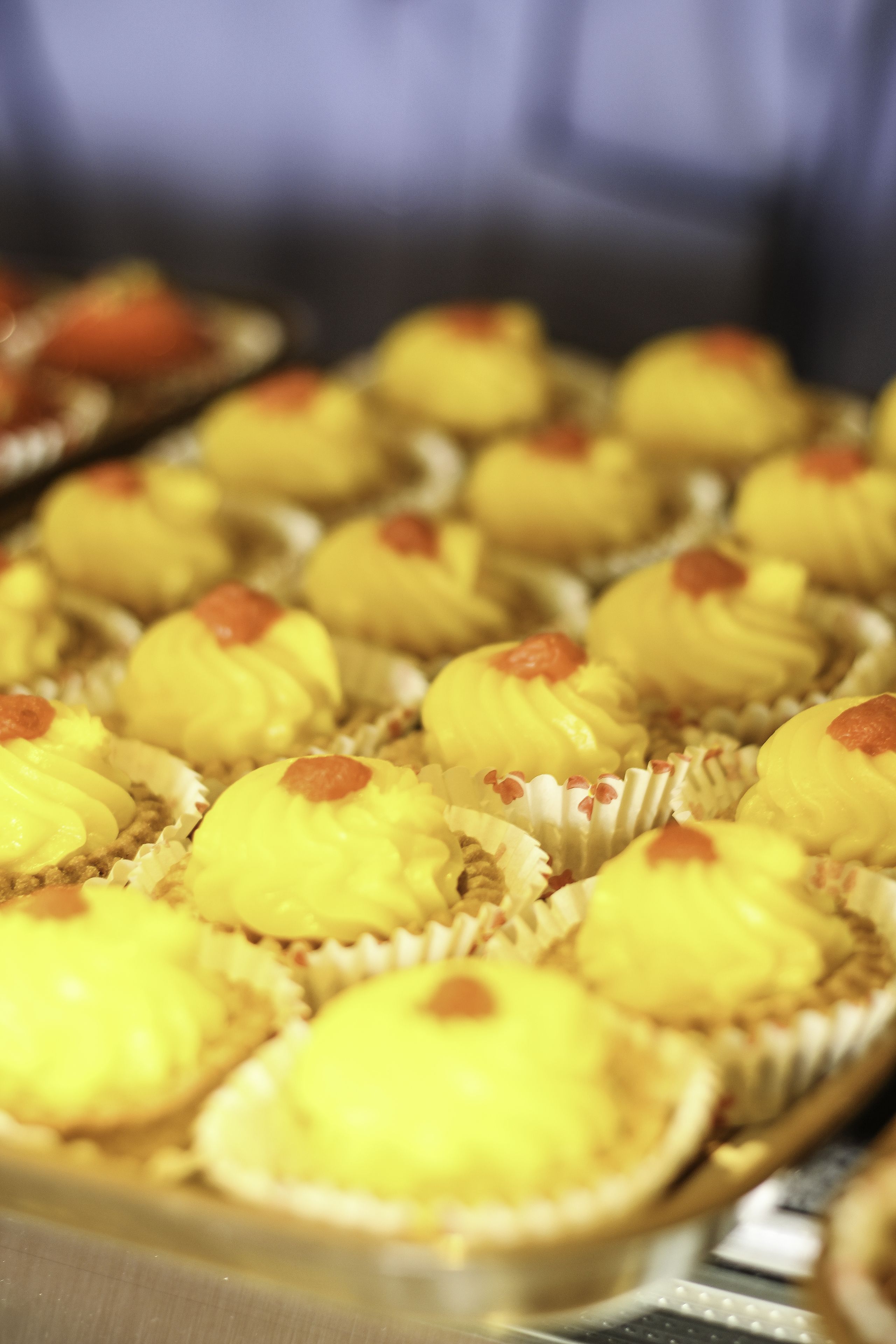 A tray of yellow cupcakes with red toppings.