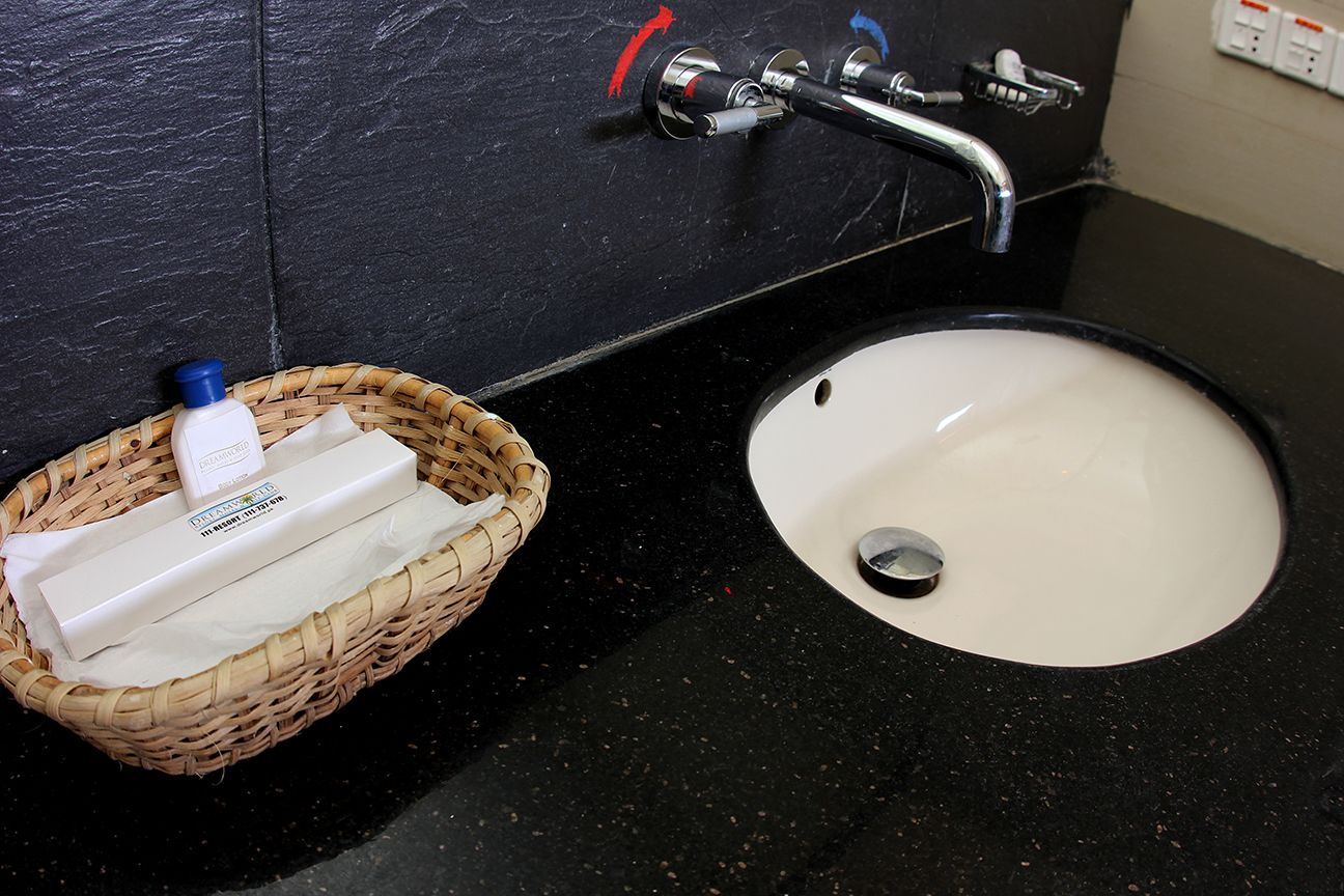 Un baño con encimera negra, lavabo blanco y una cesta de mimbre con artículos de aseo.