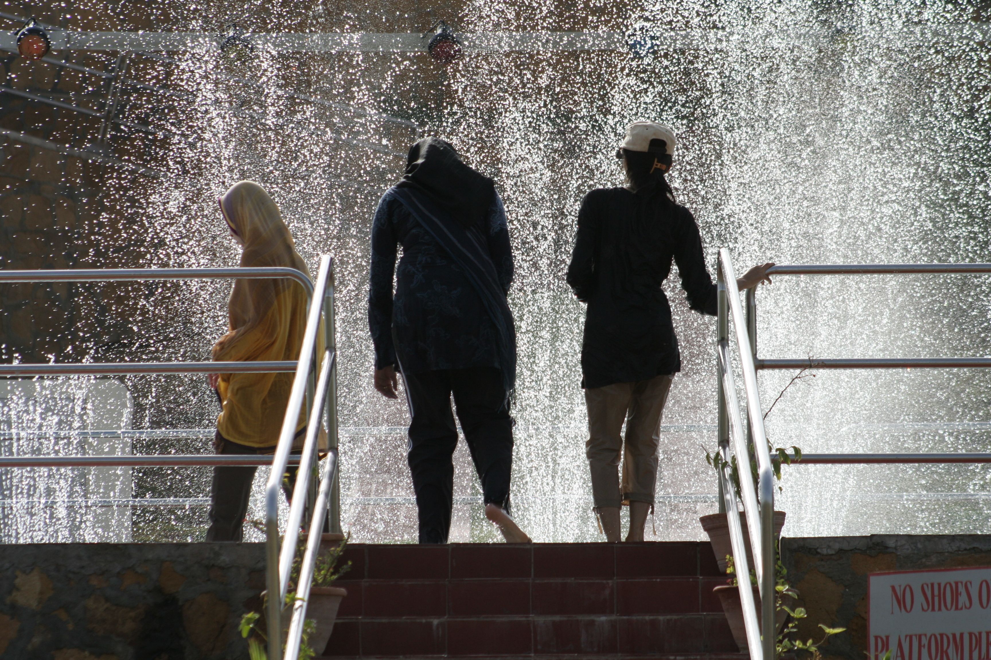 A staircase with a water feature at the top, a sign prohibiting shoes on the platform, and a metal railing.