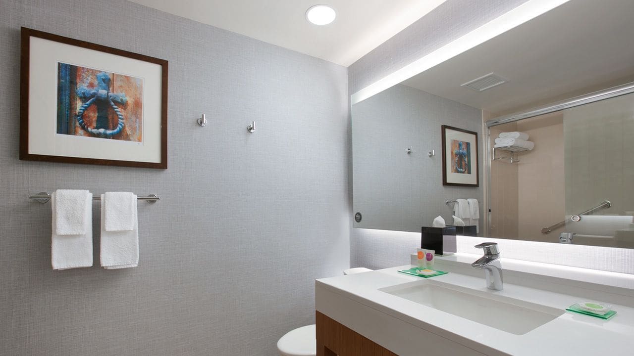 Un baño moderno con un espejo grande, un lavabo blanco y dos toallas en un perchero.