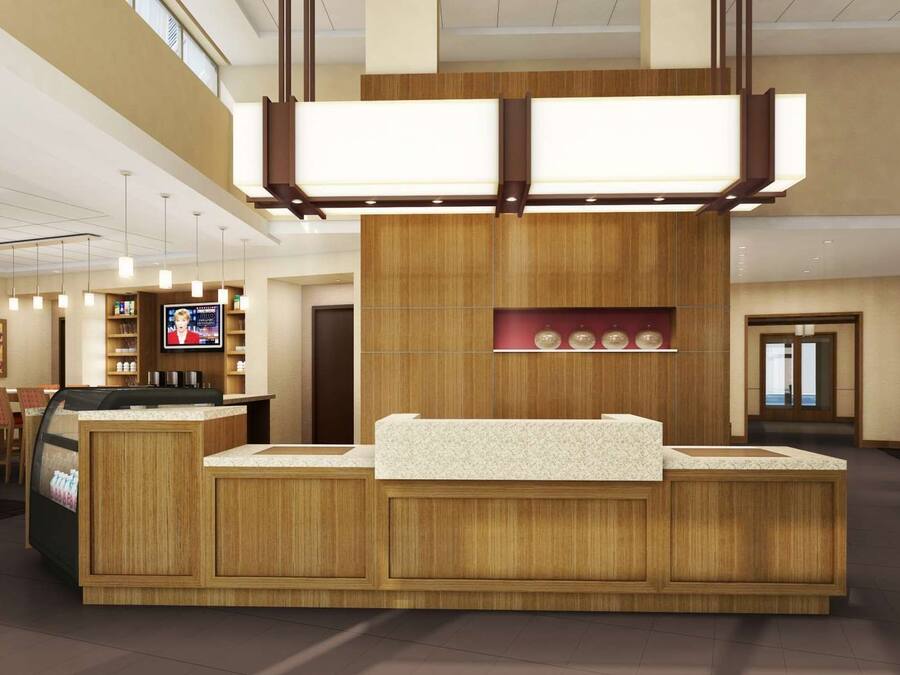 A modern hotel lobby with a reception desk, seating area, and a TV screen.