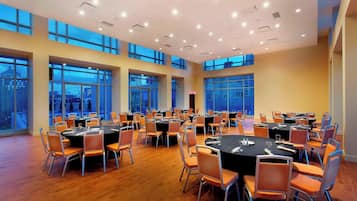 A large conference room with multiple tables and chairs, large windows, and a high ceiling with recessed lighting.