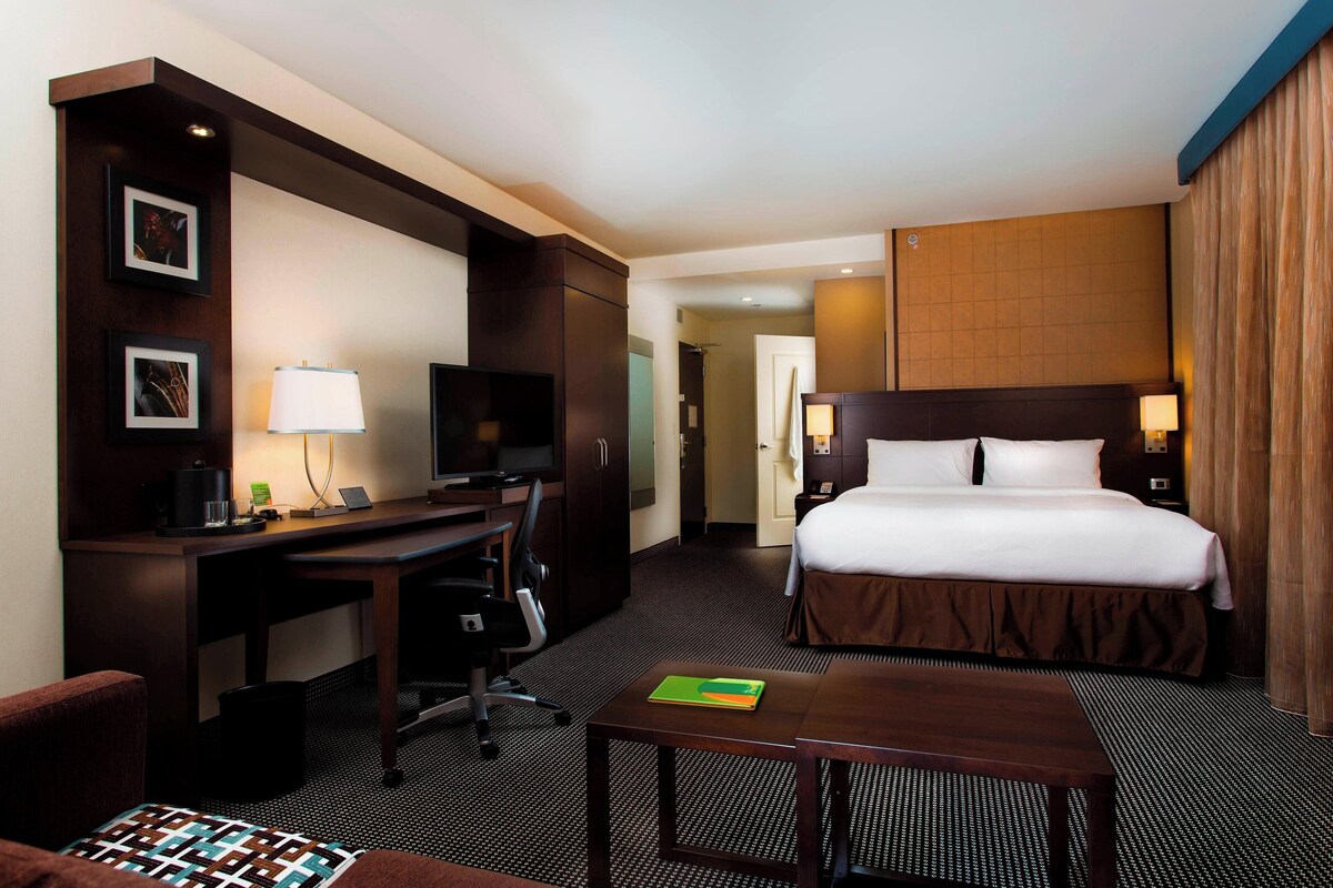 A hotel room with a bed, desk, chair, TV, and a small table.